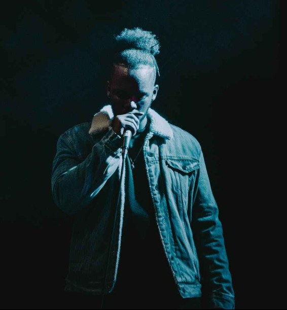 man wearing denim jacket singing on stage